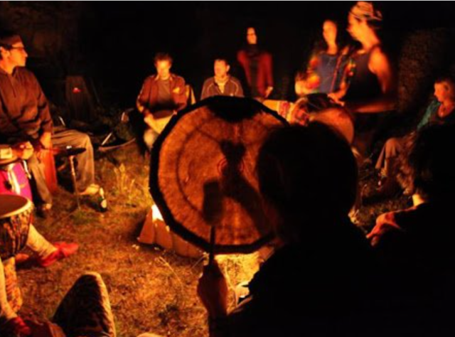 people dance around a fire while a person drums in the foreground