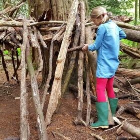 A girl adjusts a branch as she builds her own den around the trunk of a tree