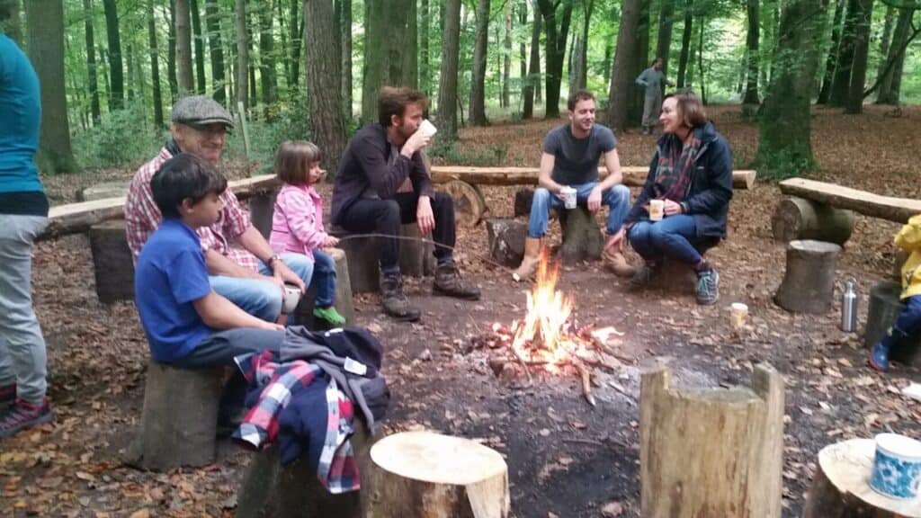 Group of people sit around a bonfire drinking tea.
