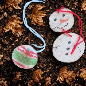 two fun handmade wooden decorations, a bauble and a snowman, sit on the forest floor