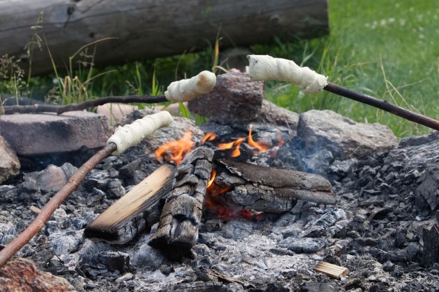 three sticks of damper bread are cooking on an open fire